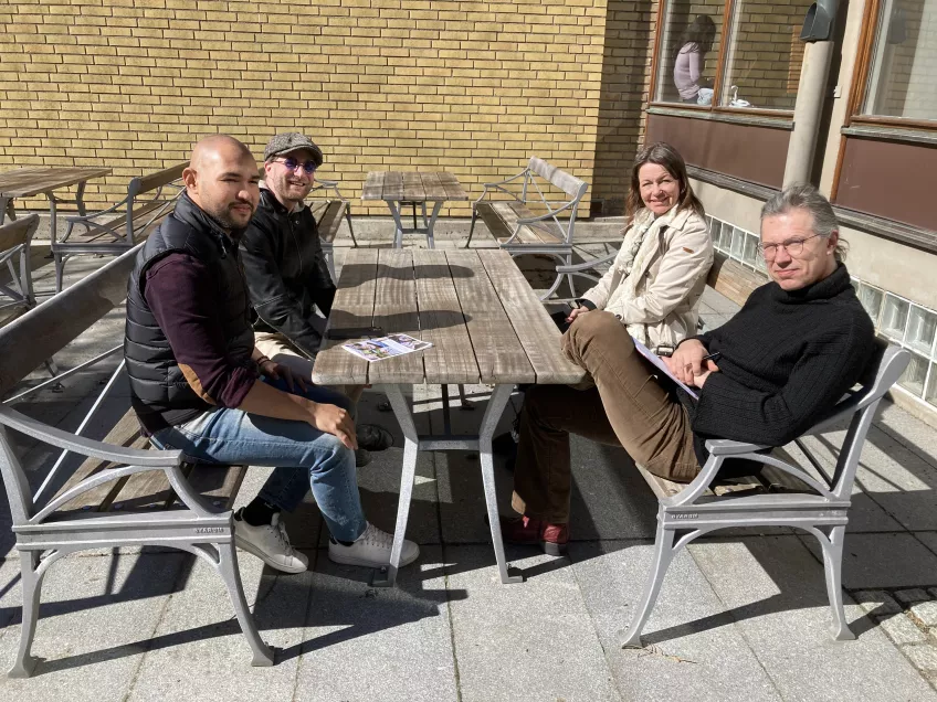 Fyra doktorander sitter vid bord ute i solskenet